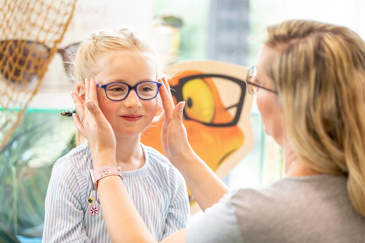 Eine Hagemann Mitarbeiterin hilft Kind bei Wahl der Brille